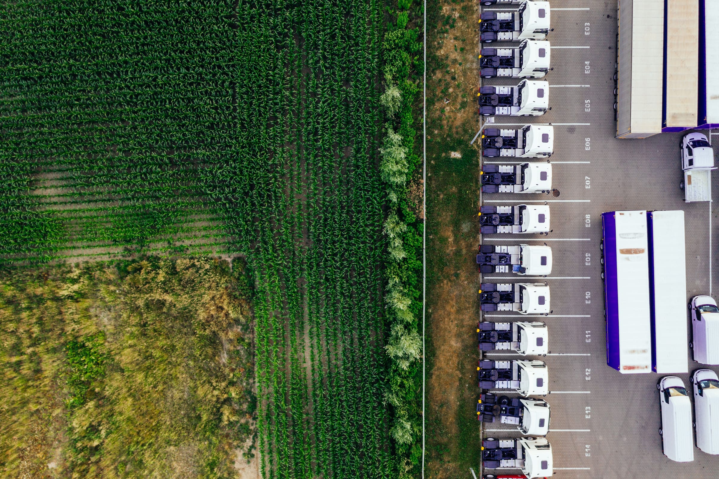 Aerial view of a crop field meeting a haulage depot, trucks lined up in their bays